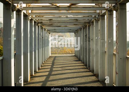 A long, empty, and narrow walkway made of metal. The walkway is devoid of any people or objects, giving it a desolate and eerie atmosphere. The metal Stock Photo