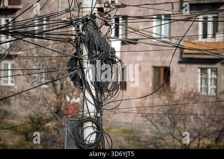 A pole with many wires on it. The wires are tangled and messy. The pole is in front of a building Stock Photo