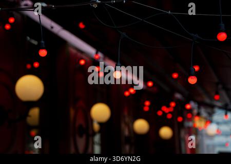 Hanging string lights with glowing red bulbs suspended on dark cables above decorative wall lamps in an atmospheric outdoor passage creating layered i Stock Photo