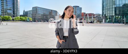 Young Asian business woman wears suit standing on city street talking on phone Stock Photo