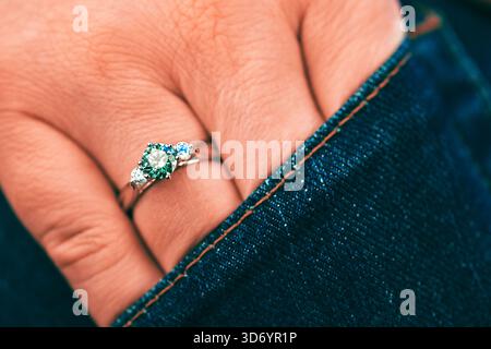 A person is wearing a ring with three stones on it. The ring is on their finger and is visible through the sleeve of their blue jeans Stock Photo