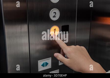 The hand of a girl kid presses an elevator button, showing a finger pushing the button inside the elevator. Stock Photo