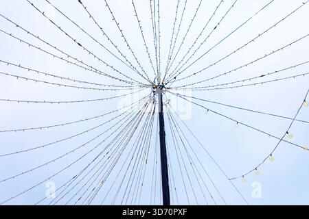 Strings of lights radiate symmetrically from a tall central pole, forming a festive canopy against pale sky. Geometric pattern creates a striking star Stock Photo