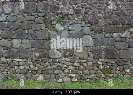 Old stone wall with weathered texture made of irregular rocks in natural daylight Stock Photo