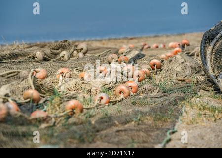 Close-up of a brown fishing net with plastic floats, laid out on the sandy beach shore on a bright, sunny day Stock Photo