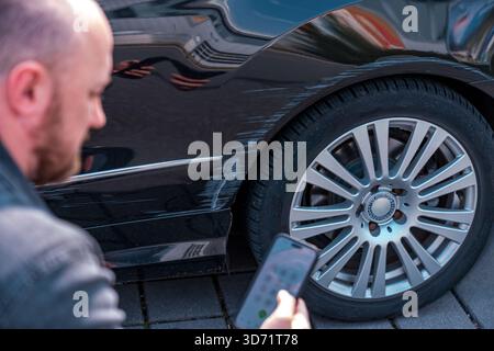 Man photographing car damage on scratched vehicle body Stock Photo