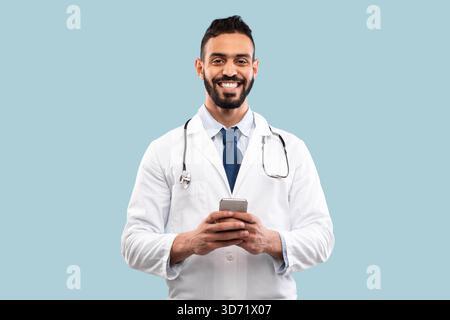 Smiling Doctor in White Coat Using Smartphone in a Bright, Simple Background Stock Photo