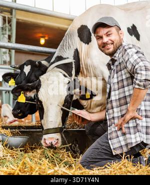 Male livestock farmer smiling and holding digital tablet while inspecting cows at cattle farm Stock Photo