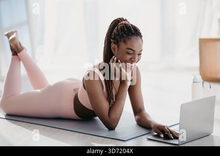 Happy Young Woman Participating in Online Fitness Class From Home on a Yoga Mat Stock Photo