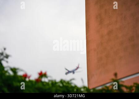 Lisbon, Portugal – A distant plane passes an orange wall above a garden on an overcast day. Stock Photo