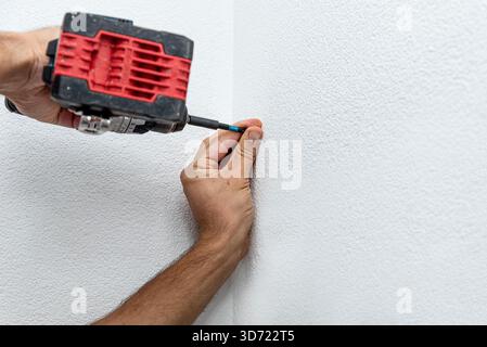 Man repairman makes hole in the wall with drill, repair work in the house with construction equipment Stock Photo