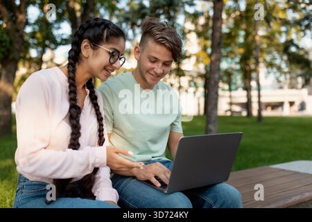 Teenagers Collaborating on a Laptop in a Sunny Park While Enjoying Their Time Outdoors Stock Photo