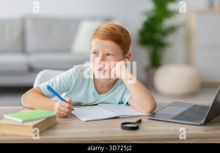 Cute Redhead Boy Daydreaming While Doing Homework at His Desk in a Cozy Home Setting Stock Photo