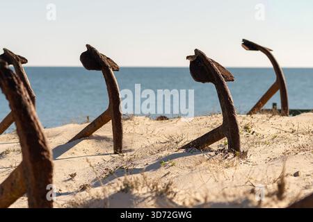 Iron anchors planted in soft dunes overlook the calm sea along the southern coast of Tavira Island. Stock Photo
