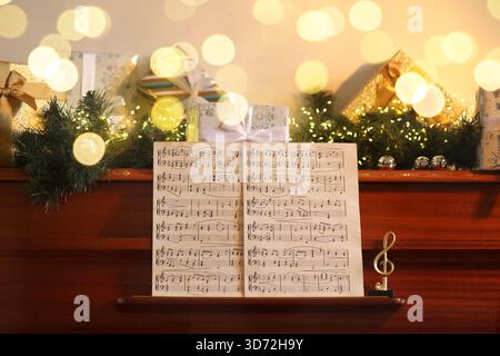 Music sheets, note and Christmas decor on piano indoors. Bokeh effect Stock Photo