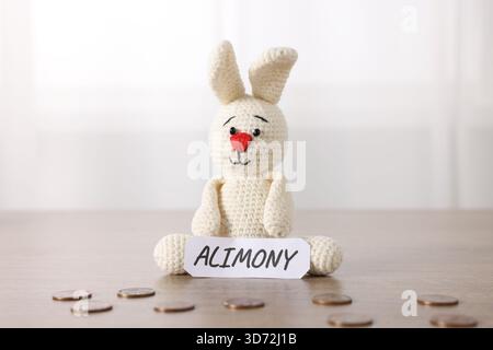 Paper note with word Alimony, toy bunny and coins on wooden table Stock Photo