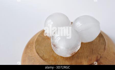 Ice balls for cocktails on wooden pedestal podium. Ice cream freezing and melting processes, minimalist scene. Ice cube melting, isolated. Frozen food Stock Photo