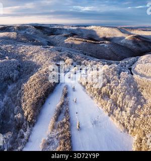 Aerial view of fairy village in snow, road, forest at winter. Top view from drone of mountain village, snowy pine trees at sunrise in Slovakia Stock Photo