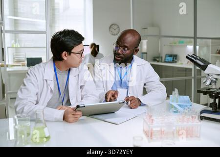 Young Adult Asian Man and Middle Aged Black Man Discussing Research in Laboratory Stock Photo
