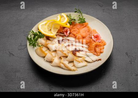Assorted smoked fish platter with salmon, lemon slices and microgreens on plate Stock Photo