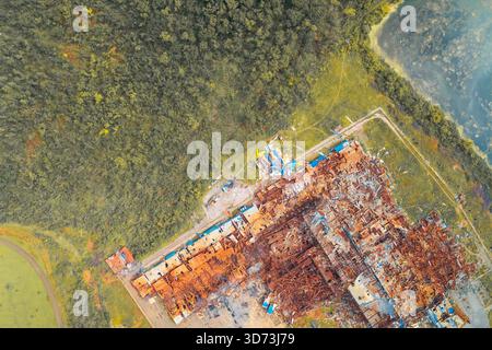 High-angle aerial view of a heavily damaged industrial complex and factory building, destroyed as a result of the Russian invasion of Ukraine. Site located near water and forest. Stock Photo
