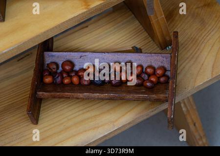 A small, wooden, rectangular container is filled with brown seeds or small fruits, possibly dates. It is set on a light wooden surface. Stock Photo