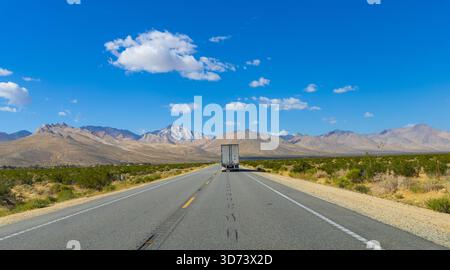 The desolate US Route 395 highway stretching toward the horizon in the Eastern Sierra region of California. In the distance there's an abandoned truck. Stock Photo