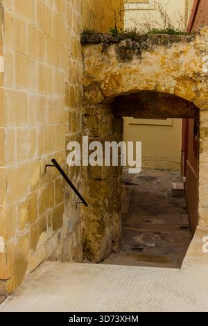 Old Stone Archway Over Narrow Sunlit Alleyway in Historic European Passage Stock Photo