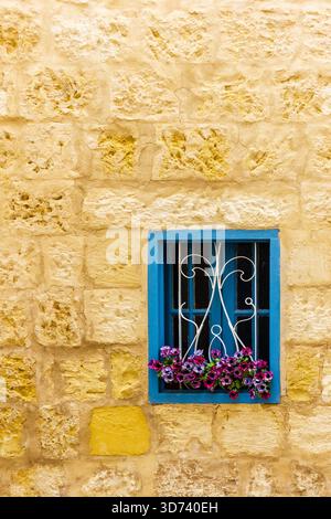 Bright Blue Window With Ornate White Grilles And Colorful Flower Box On Yellow Stone Wall Stock Photo