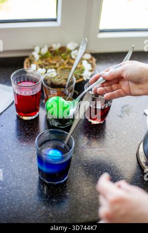 A variety of brightly colored Easter eggs sit in glasses with spoons. Easter preparations. Stock Photo