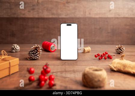 Smartphone standing upright in Christmas flat lay scene with pinecones and berries, ideal for app mockups, product showcases and holiday marketing vis Stock Photo