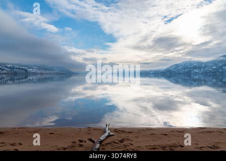 Sun shining through the clouds with a view of snow-covered mountains and sandy beach at Skaha Lake, Penticton, BC, Canada Stock Photo