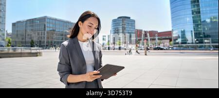 Young happy Asian business woman standing on city street using digital tablet Stock Photo