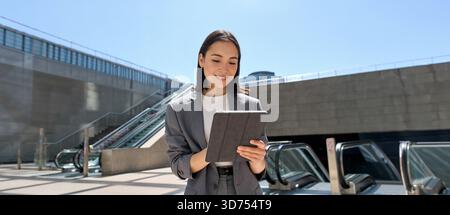 Smiling Asian young business woman standing in city subway using tablet Stock Photo