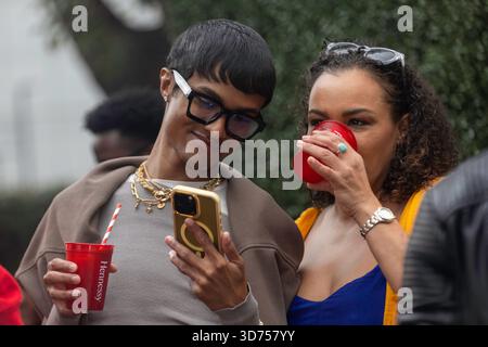 This is a stylish, candid photograph capturing a moment between two people at an outdoor social event. a woman is seen taking a sip from a second red Stock Photo