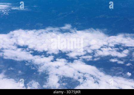 Layer of white cumulus clouds contrasting against blue sky and glimpses of terrain below. Perspective from altitude, looking down over horizontal band Stock Photo