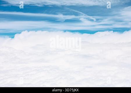 Aerial perspective of vast, fluffy white cloud layer that blankets lower half of the image. Above this dense formation blue sky with some wispy high-a Stock Photo