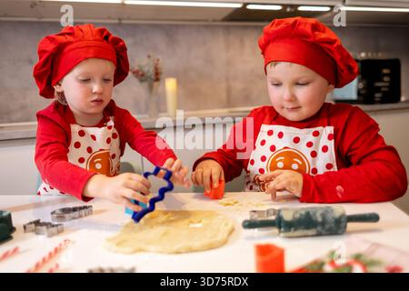 Two children are engaged in a fun baking activity, using cookie cutters to shape dough on a kitchen counter. Their joyful expressions show their excit Stock Photo