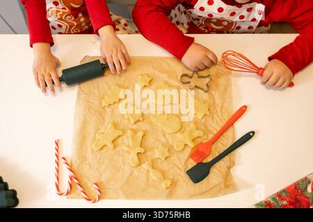 Two children engage in decorating holiday cookies with various shapes on a table. The kitchen is festive, filled with cookie cutters and other baking Stock Photo