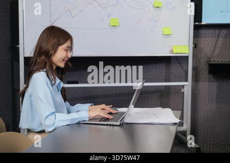 Young Asian business woman busy typing on laptop, actively working on project in modern meeting Stock Photo