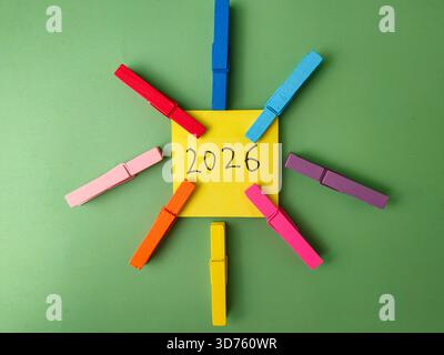 The image is a stock photo concept featuring a yellow sticky note with 2026 written on it, surrounded by colorful clothespegs. Stock Photo