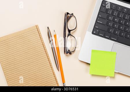 Blank notepad, laptop and stationery on beige workspace, top view with copy space, minimal office background Stock Photo