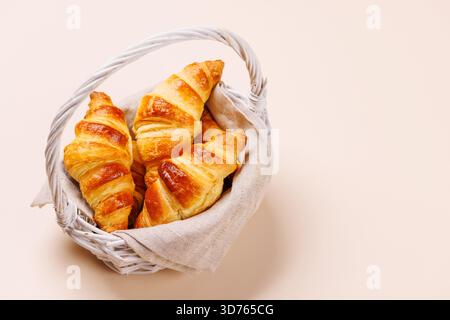 Freshly baked croissants in wicker basket on light background, cozy breakfast Stock Photo