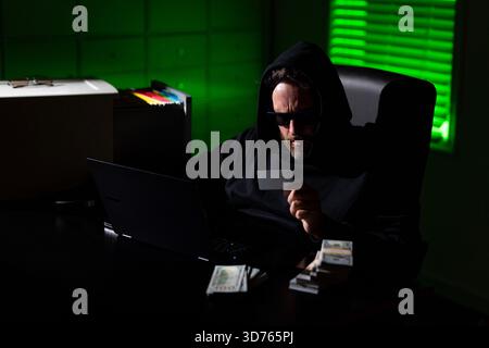 Hacker in a night office during a cyber attack. Hacker stolen crypto currency. Digital money hacker. Cyber attack. Hacker in a hoodie using laptop in Stock Photo