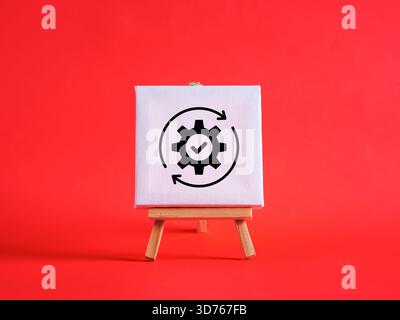 Optimizing processes with a rotating gear and check mark on a small canvas against a red background, symbolizing efficient workflow and process manage Stock Photo