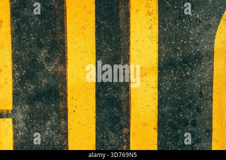 Top view of yellow road marking lines painted on a dark asphalt surface as abstract background Stock Photo