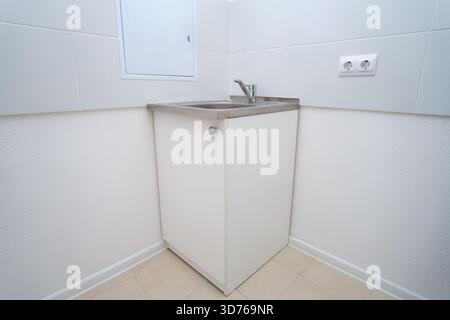 Small stainless steel sink cabinet with a modern faucet in a white tiled utility room. Clean and functional interior for kitchen or laundry. Stock Photo