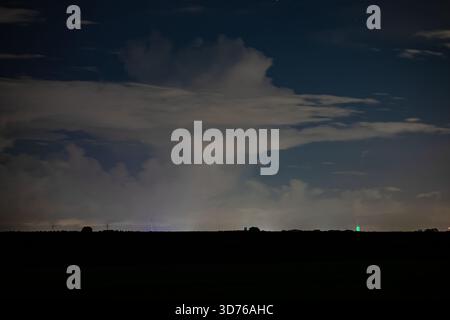 Distant thundery shower illuminating the night sky over dark open plain land Stock Photo