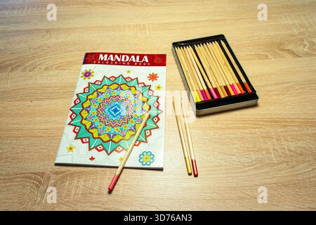 Mandala coloring book with pencils arranged on wooden table for creative relaxation. Stock Photo