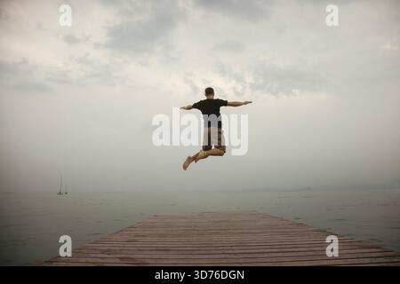 Boy jumping high on the pier in front of the sea in a gesture of pure freedom Stock Photo